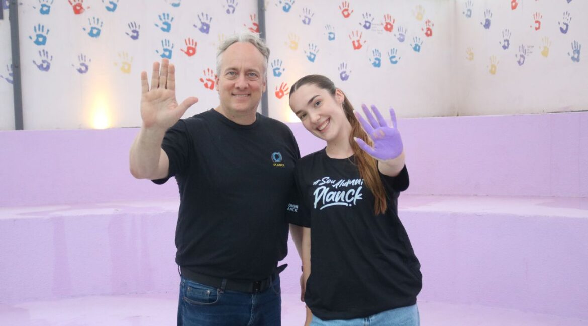 Diretor Umberto Malanga e ex-aluna Giovana Lorenzi em momento alegre no mural de mãos coloridas do Colégio Planck.