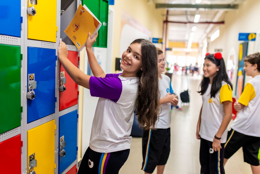 Estudante menina guardando material escolar em armário.