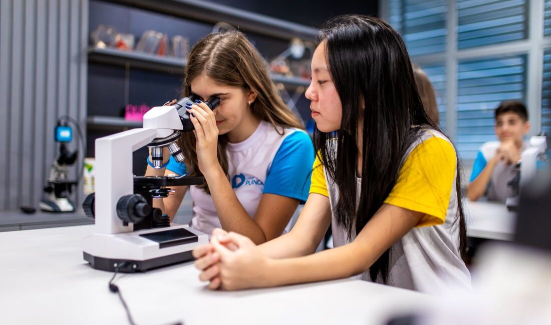 Estudantes olhando em microscópio em laboratório de ciências de colégio.