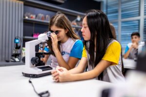 Estudantes olhando em microscópio em laboratório de ciências de colégio.