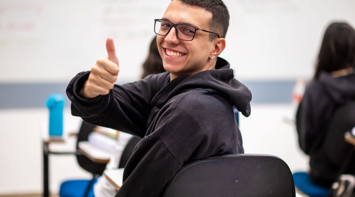 Estudante do ensino médio virado para trás fazendo sinal de joinha.