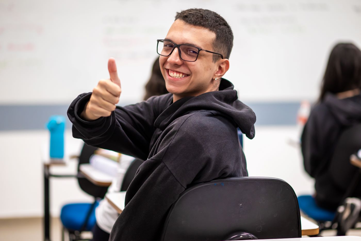 Estudante do ensino médio virado para trás fazendo sinal de joinha.