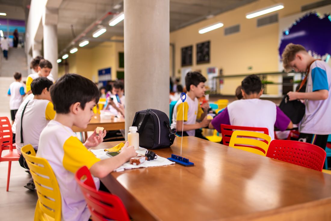 Estudantes se alimentando de lanches saudáveis em refeitório do Colégio Planck durante intervalo.