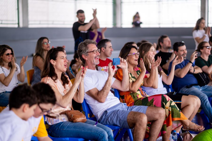 Pais de estudantes e filhos sentados para assistir apresentação.