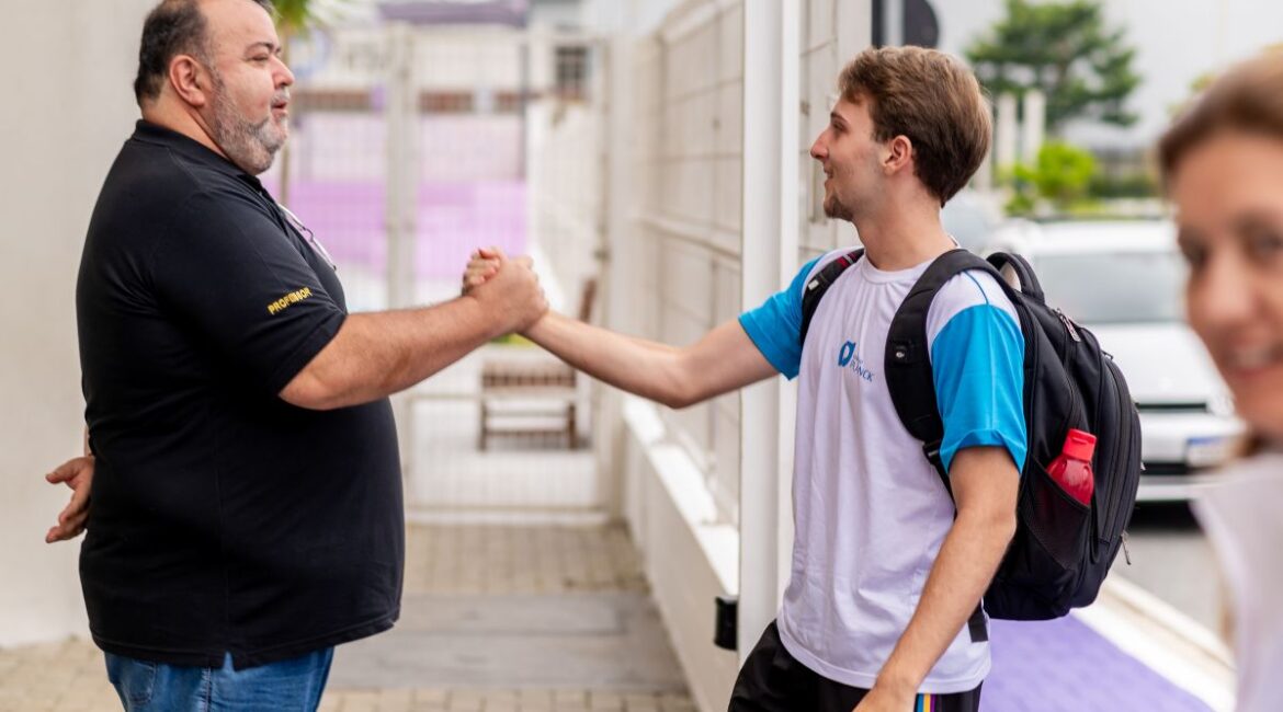 Estudante chegando em escola e cumprimentando professor.