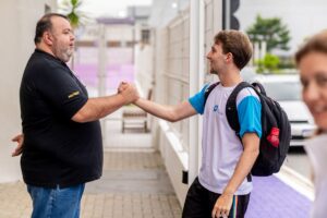 Estudante chegando em escola e cumprimentando professor.