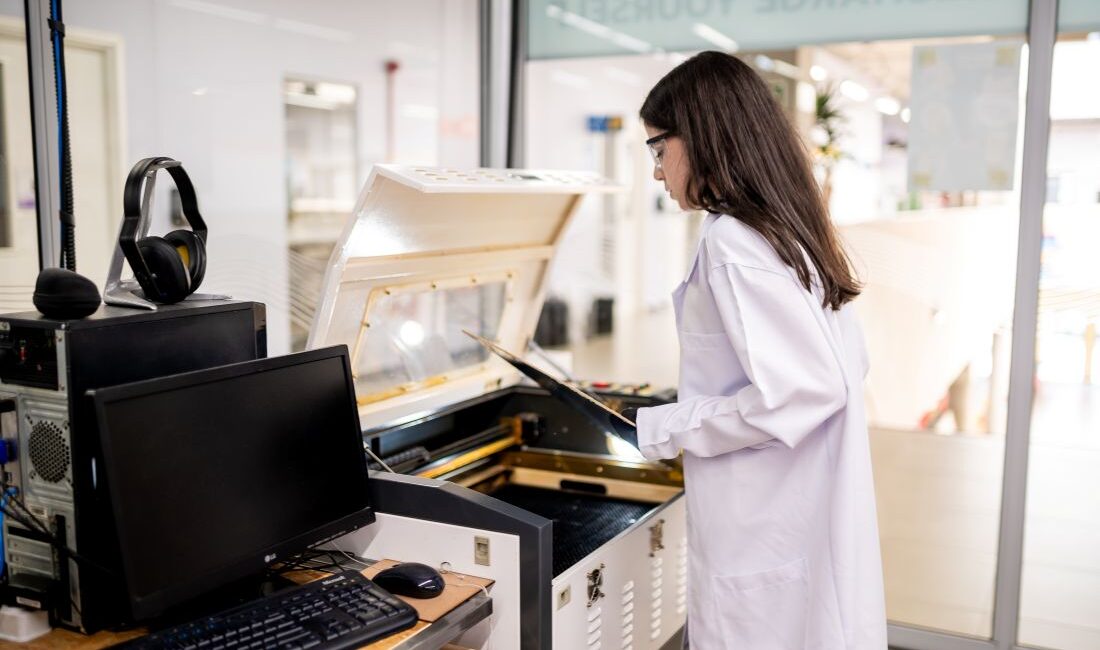 Estudante manuseando máquina de corte a laser em laboratório escolar moderno, representando o protagonismo, a tecnologia e o aprendizado prático no Colégio Planck.
