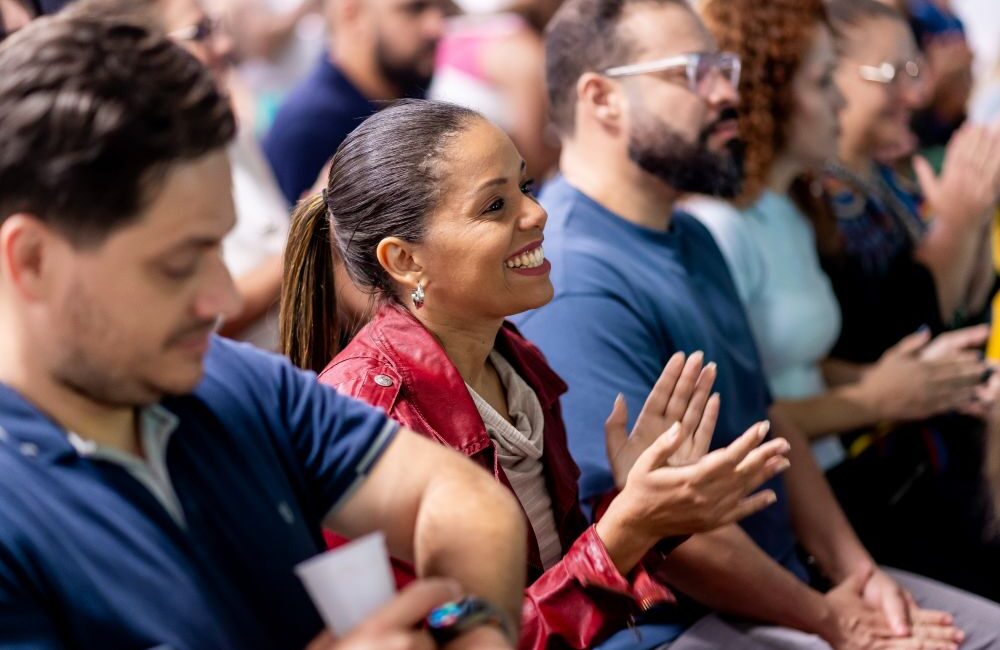 Pais engajados aplaudem evento escolar, simbolizando como a presença familiar impacta positivamente o desempenho dos filhos.