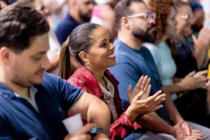 Pais engajados aplaudem evento escolar, simbolizando como a presença familiar impacta positivamente o desempenho dos filhos.