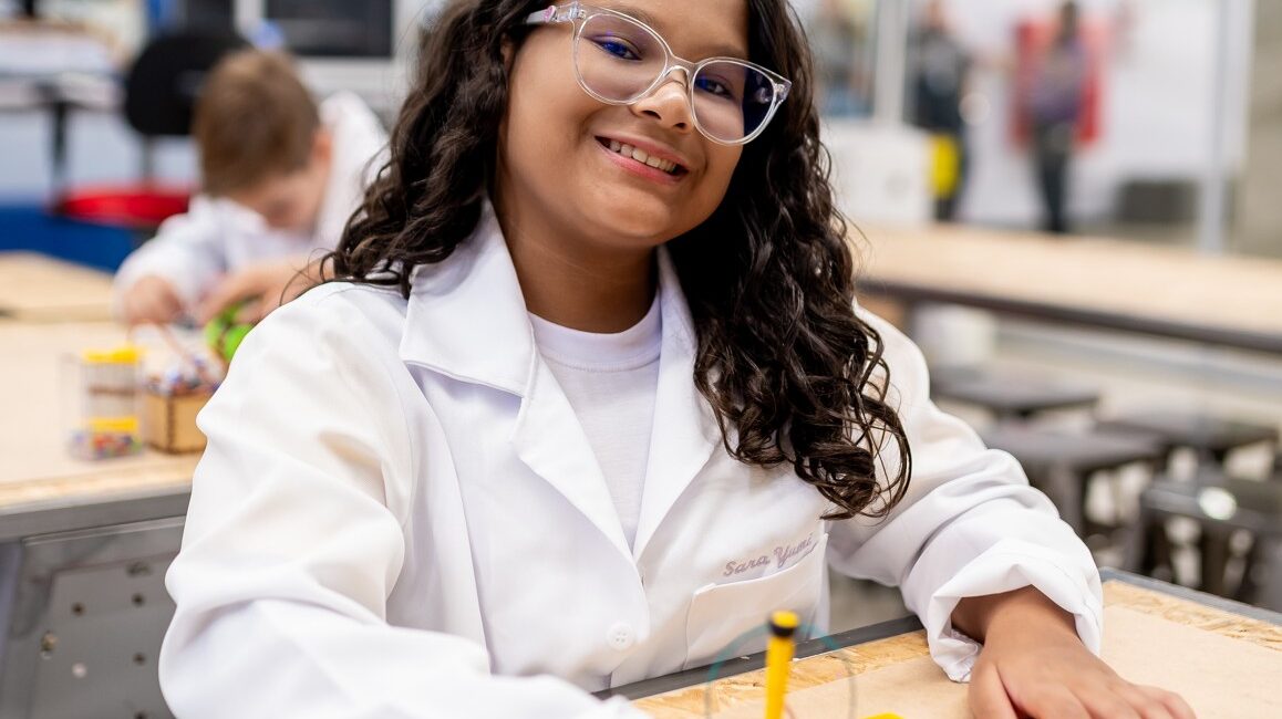 Estudante no laboratório do Colégio Planck com jaleco e óculos de proteção, representando o ensino experimental desde o 6º ano.