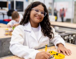 Estudante no laboratório do Colégio Planck com jaleco e óculos de proteção, representando o ensino experimental desde o 6º ano.