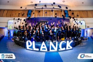Estudantes do Colégio Planck comemoram aprovações em universidades lançando capelos no palco em evento oficial de formação.