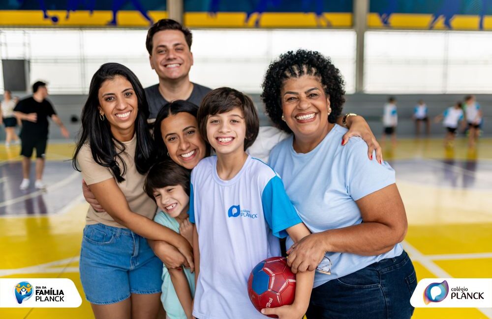 Grupo de adultos e crianças sorrindo e abraçados durante o Dia da Família do Colégio Planck, participando de atividades propostas pelo colégio familiar.
