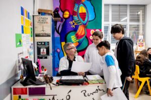 Três estudantes conversam com um professor, participando de uma atividade de estudo ativo, com diálogo e troca de ideias para compreender e aplicar o conteúdo de forma prática e colaborativa.