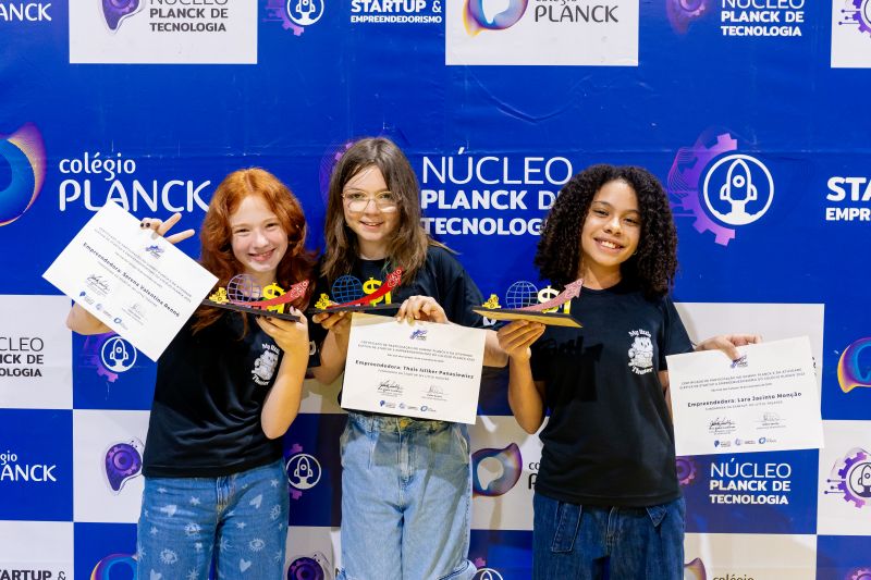Três estudantes do Colégio Planck sorrindo e segurando certificados d