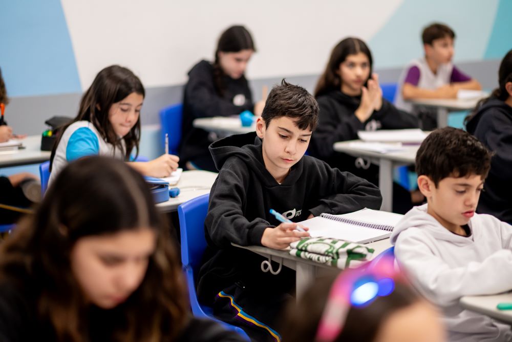 Estudantes do Colégio Planck concentrados em sala de aula, organizando cadernos e materiais durante a rotina estruturada de estudos no Ensino Fundamental II.
