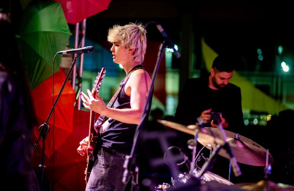 Estudante toca guitarra e canta em apresentação musical com banda, em ambiente escolar que estimula educação e criatividade no Colégio Planck.