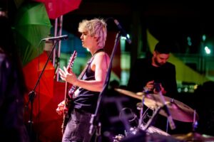 Estudante toca guitarra e canta em apresentação musical com banda, em ambiente escolar que estimula educação e criatividade no Colégio Planck.