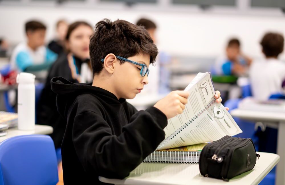Estudante concentrado lendo material didático em sala de aula, ilustrando os sinais que mostram se seu filho está pronto para o 6º ano além das notas.
