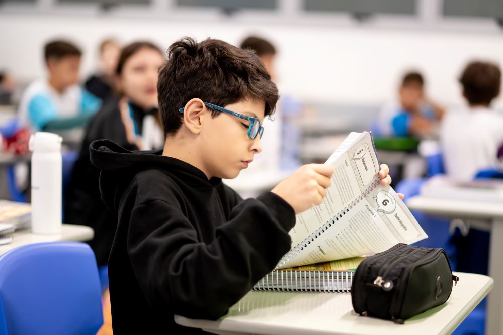 Estudante concentrado lendo material didático em sala de aula, ilustrando os sinais que mostram se seu filho está pronto para o 6º ano além das notas.
