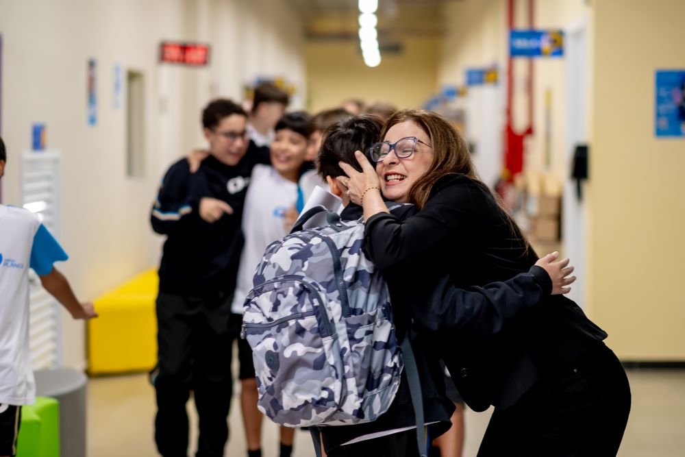 Educadora abraça estudantes em corredor escolar, representando como o 6º ano é uma mudança acadêmica ou emocional na adaptação dos estudantes.