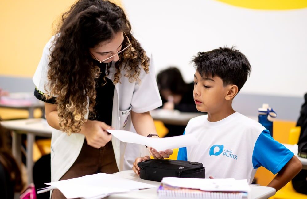 Professora auxilia aluno em atividade escolar, ilustrando por que o 6º ano marca uma nova etapa na vida escolar.