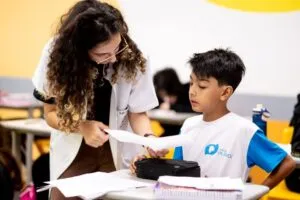 Professora auxilia aluno em atividade escolar, ilustrando por que o 6º ano marca uma nova etapa na vida escolar.