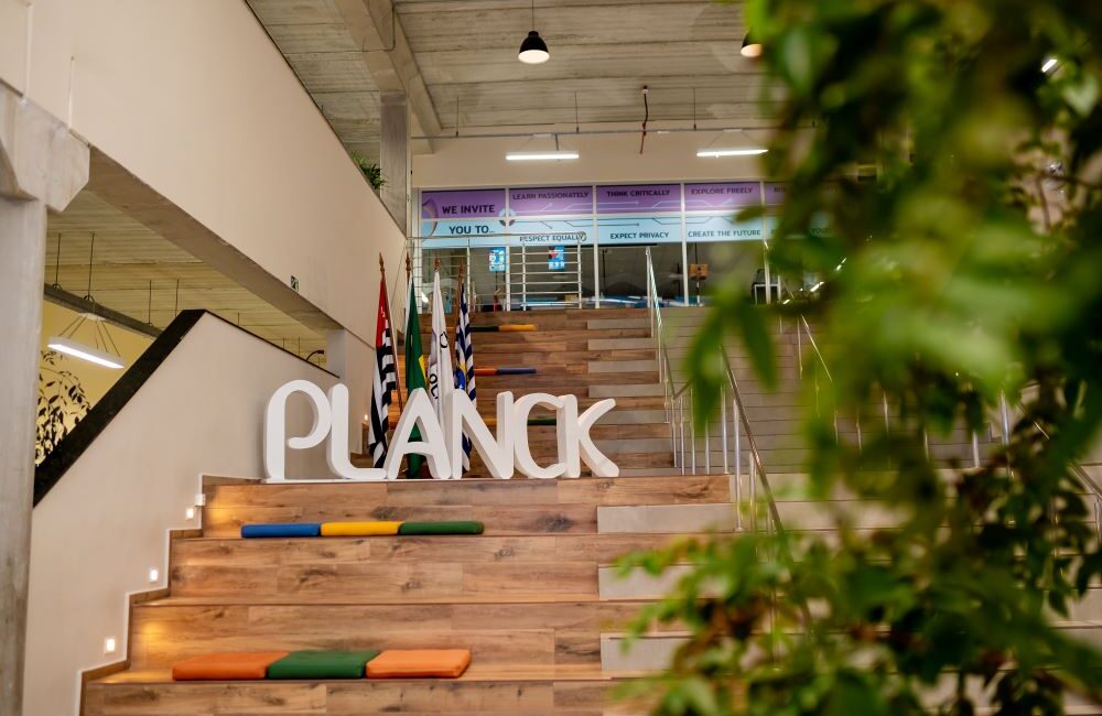 Ambiente interno do Colégio Planck com escadaria, área de convivência e identidade visual da instituição, representando crescimento, excelência acadêmica e destaque no Enem 2025.