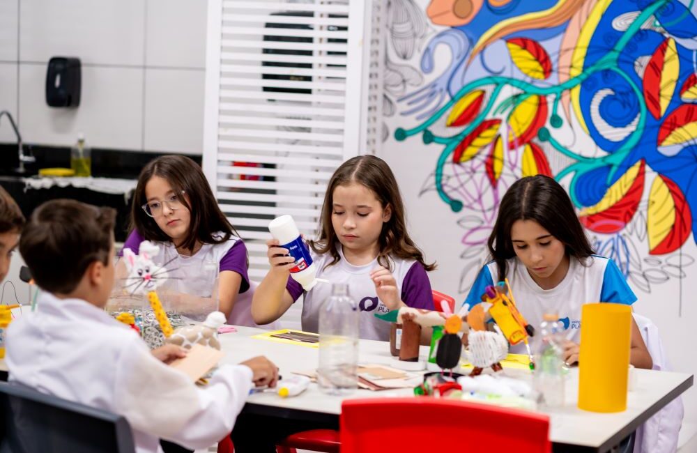 Crianças participam de uma oficina criativa utilizando materiais diversos para desenvolver projetos, representando a criatividade como uma habilidade treinável e essencial para o futuro.