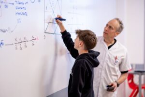 Estudante resolve exercício de matemática na lousa com orientação do professor, representando como o erro faz parte da aprendizagem e isso tem explicação científica.