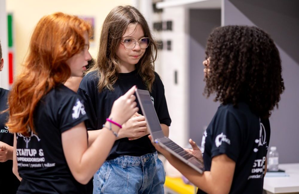 Estudantes do Colégio Planck participando da extracurricular de Startup e Empreendedorismo, analisando um projeto em notebook, desenvolvendo autonomia, protagonismo e letramento tecnológico.
