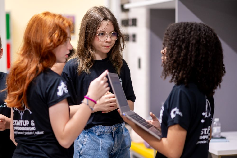 Estudantes do Colégio Planck participando da extracurricular de Startup e Empreendedorismo, analisando um projeto em notebook, desenvolvendo autonomia, protagonismo e letramento tecnológico.
