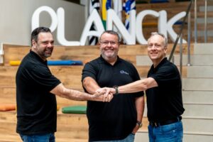 Três homens sorrindo e unindo as mãos em comemoração aos 10 Anos do Colégio Planck.