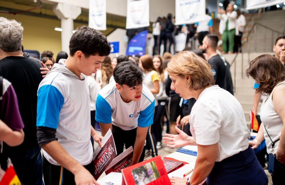 Estudantes do Colégio Planck conversando com representante de universidade em feira de profissões, buscando repertório para a escolha da carreira no Ensino Médio.